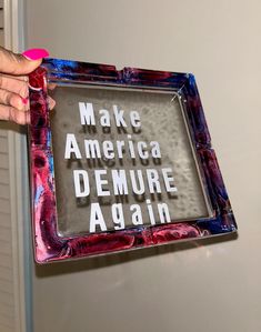 a person holding up a sign that says make america demure again