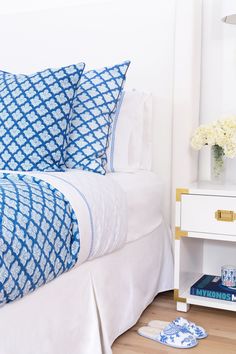 a bed with blue and white pillows on top of it next to a night stand