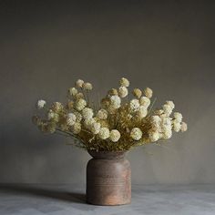 a vase filled with lots of white flowers on top of a gray table next to a wall