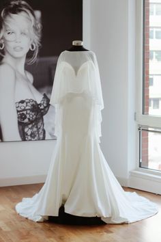 a white wedding dress on display in front of a window with a black and white photo behind it