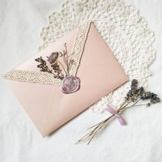 an envelope and some flowers on a lace doily next to a piece of pink paper