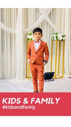 a young boy in an orange suit and bow tie standing next to a white backdrop