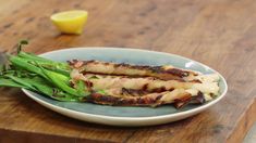 a plate with meat and asparagus sitting on a wooden table next to a lemon wedge