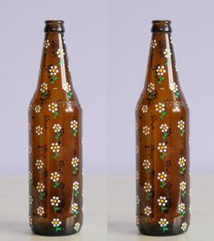 two brown beer bottles with white flowers painted on the top and bottom one is empty