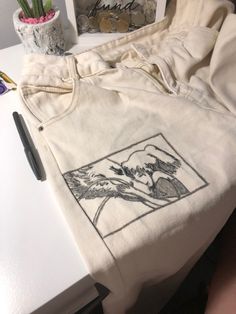 a white t - shirt sitting on top of a table next to a pen and potted plant