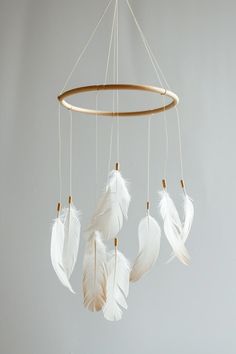 three white feathers are hanging from a circular wooden frame on a gray background, with gold accents