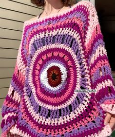 a woman wearing a pink and purple crocheted blanket with an eyeball in the center