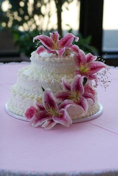 a three tiered cake with pink flowers on the top is sitting on a table