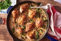 a pan filled with chicken and mushrooms on top of a wooden table next to a glass of wine