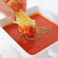 a person dipping some food into a small white bowl filled with red sauce and cheese