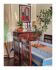 a dining room table with blue and white cloths on it, surrounded by potted plants