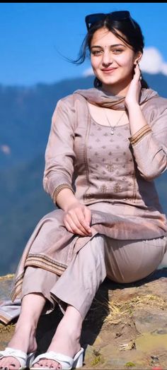 a woman sitting on top of a rock talking on a cell phone with mountains in the background