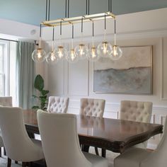 a chandelier hanging over a dining room table with white chairs and beige upholstered chairs