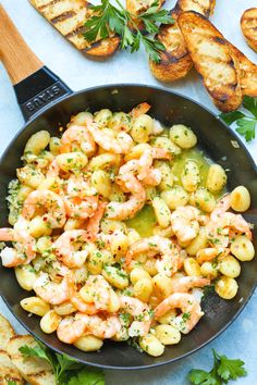 a skillet filled with shrimp and potatoes next to toasted bread on a table