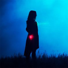 a woman standing in the grass with her back turned to the camera, holding a red light