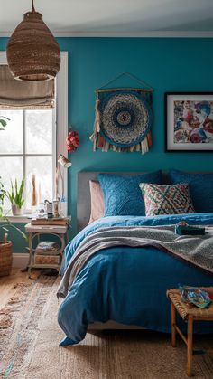 a bed with blue sheets and pillows in a bedroom next to a large window that has potted plants on it