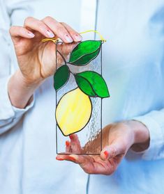 a woman holding up a stained glass vase with lemons and leaves on it in her hands