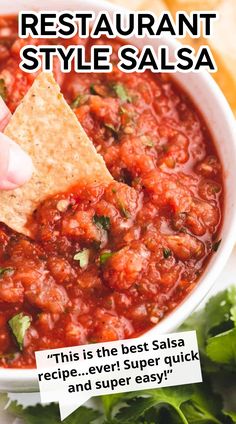 a hand holding a tortilla chip and dipping it into a bowl of salsa