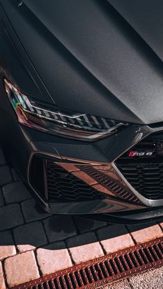 the front end of a black sports car parked on a brick sidewalk with red bricks