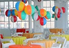 many colorful balloons are hanging from the ceiling in a room filled with tables and chairs