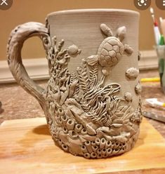 a ceramic mug sitting on top of a wooden table next to pencils and markers