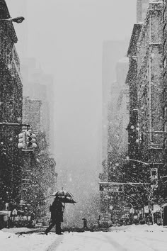 a person holding an umbrella in the middle of a snowy street with tall buildings on both sides