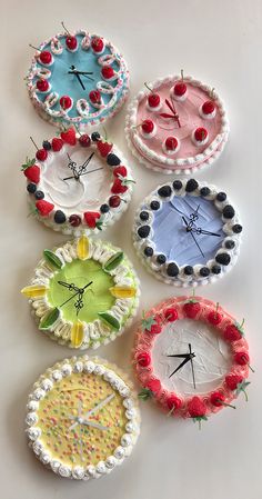 four clocks made out of paper plates with flowers and berries on the sides, all decorated in different colors