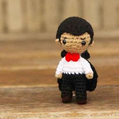 a small crocheted doll wearing a red bow tie and white dress with black hair