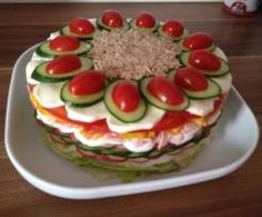 a layered cake with cucumbers, tomatoes and other toppings on a plate