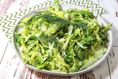 a white bowl filled with lettuce on top of a wooden table next to a green napkin