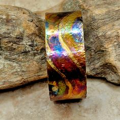 a colorful ring sitting on top of a rock next to a tree trunk and rocks