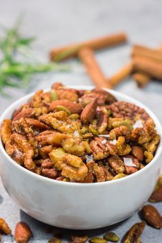 a white bowl filled with nuts on top of a table next to some cinnamon sticks