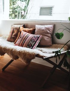 a couch with pillows on top of it in front of a window and potted plant