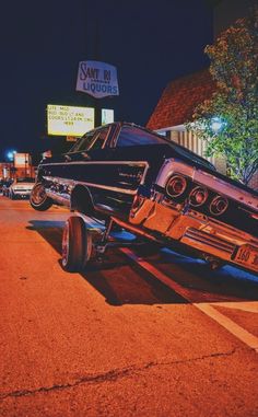 an old car is parked on the side of the road in front of a liquor store