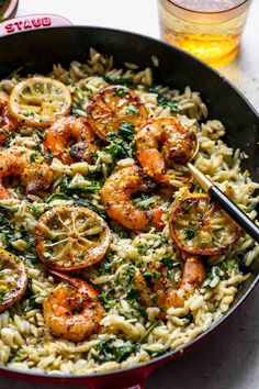 shrimp and spinach pasta in a red skillet next to a glass of beer