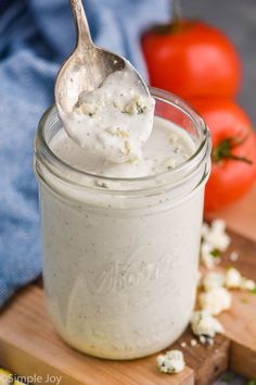 a spoon full of yogurt sitting on top of a cutting board with tomatoes in the background