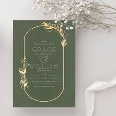 a green and gold wedding card with white flowers on the top, next to a bouquet of baby's breath