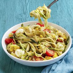 a white bowl filled with pasta and vegetables on top of a blue table cloth next to a fork