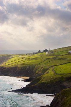 an ocean view with green grass and houses on the hill next to the water's edge