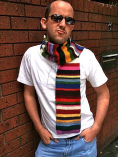 a man standing in front of a brick wall wearing sunglasses and a multicolored scarf