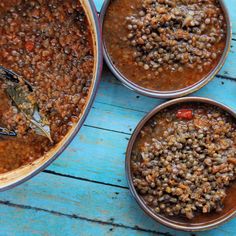 three bowls filled with food sitting on top of a blue wooden table next to two spoons