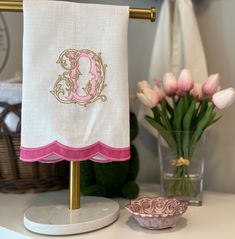 a pink and gold monogrammed towel on a stand next to a vase with tulips