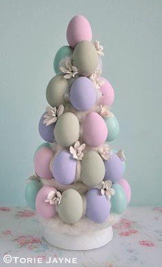 an easter tree with pastel colored eggs on top and flowers around the base, sitting on a table