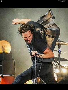 a man is performing on stage with his hands in the air as he stands next to drums