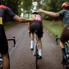 three bicyclists are riding down the road and one is holding something in his hand