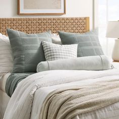 a bed with pillows and blankets on it in front of a wall hanging above the headboard