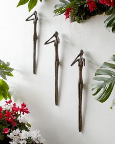 three metal birds are hanging on the wall next to potted plants and red flowers