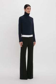 a woman wearing black pants and a turtle neck sweater, standing in front of a white background