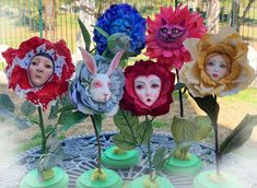 four fake flowers with faces on them sitting on a table in front of a fence