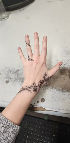 a woman's hand with a flower tattoo on her left wrist and the middle finger